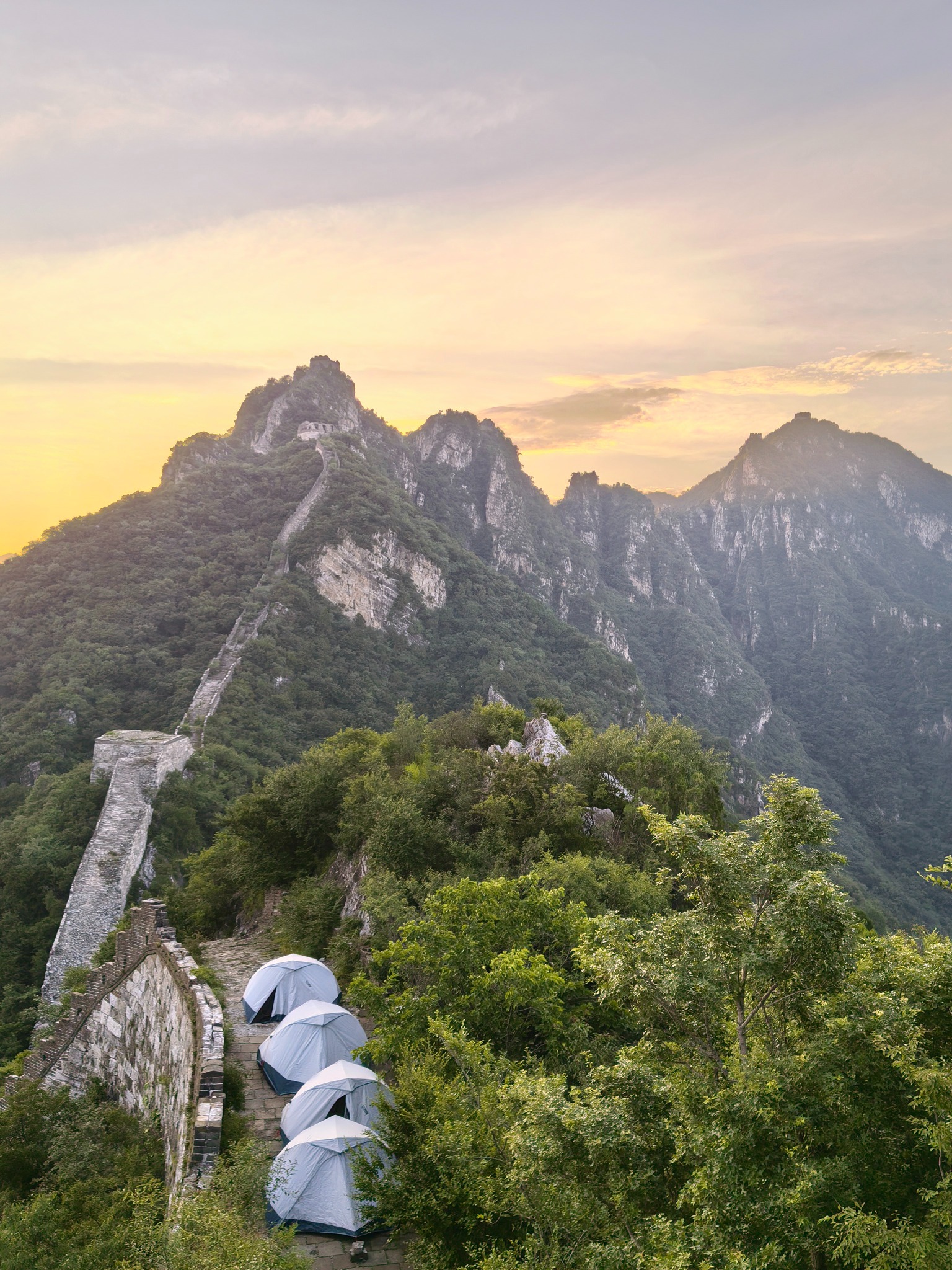 Tents along the Great Wall beneath rugged mountain ridges at sunset